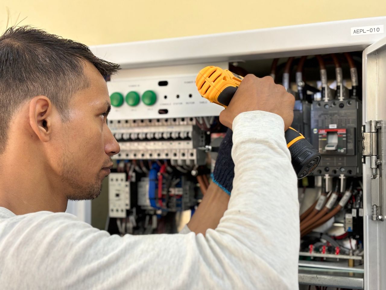 our-stories Professional electrician using a drill on an indoor circuit breaker panel.