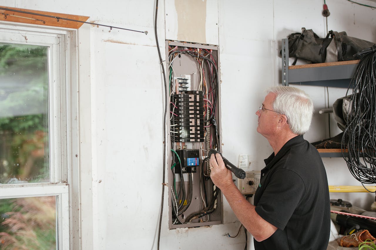 service-04 An electrician carefully examines a residential fuse box indoors, ensuring electrical safety and compliance.
