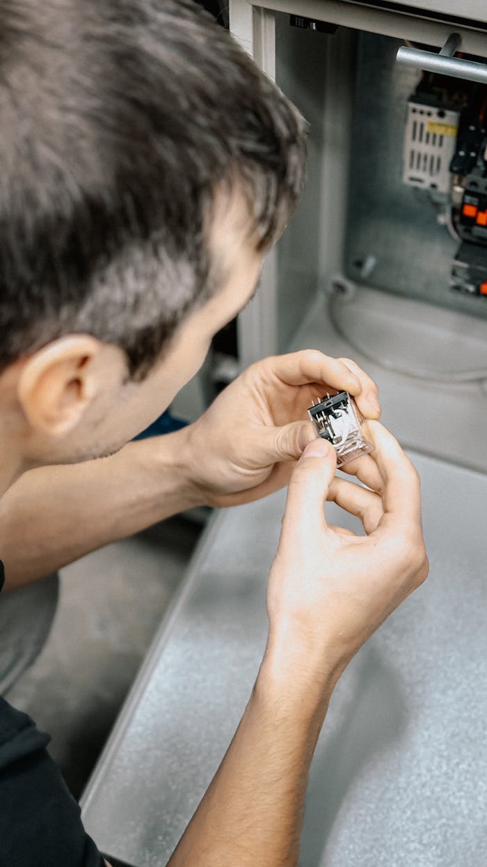 service-05 Technician carefully examining an electronic part inside a machinery panel.