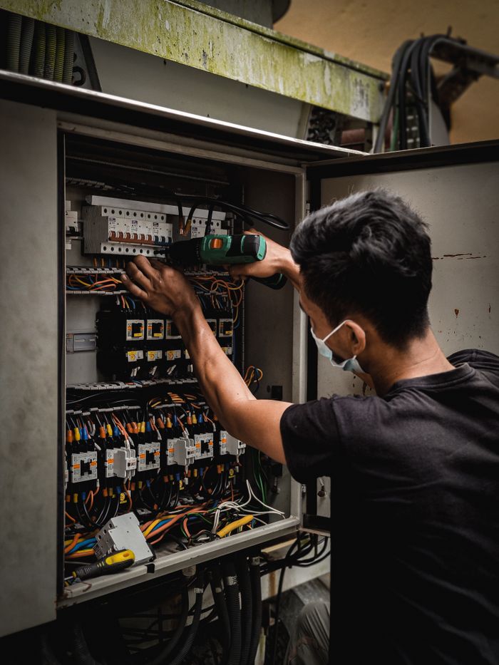 service-02 Technician working on circuit breaker panel, adjusting electrical wires indoors.